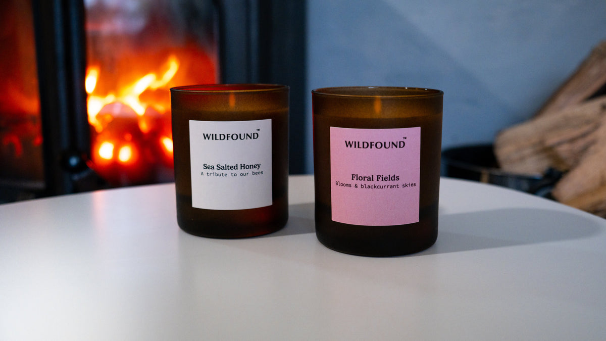 Two soy wax candles infront of a lighting fire in yellow and pink label