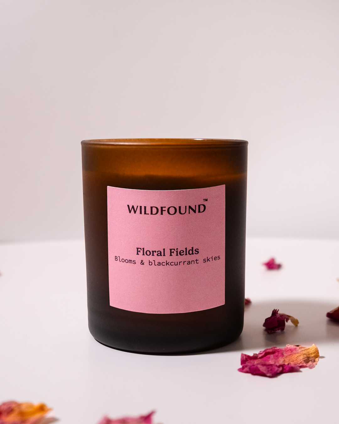 Candle with a pink label reading 'Wildfound Floral Fields' on a white background with dried flowers.