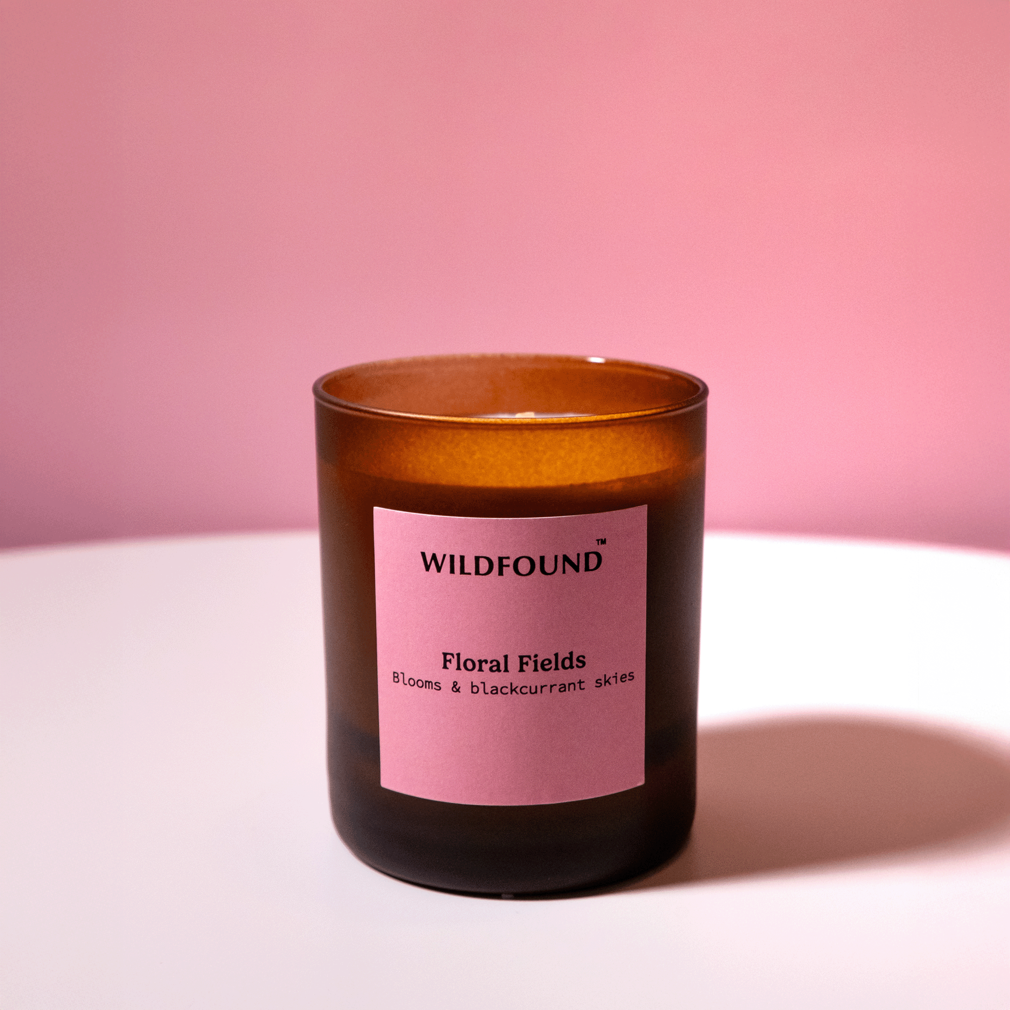 Candle with a pink label on a white surface and pink background