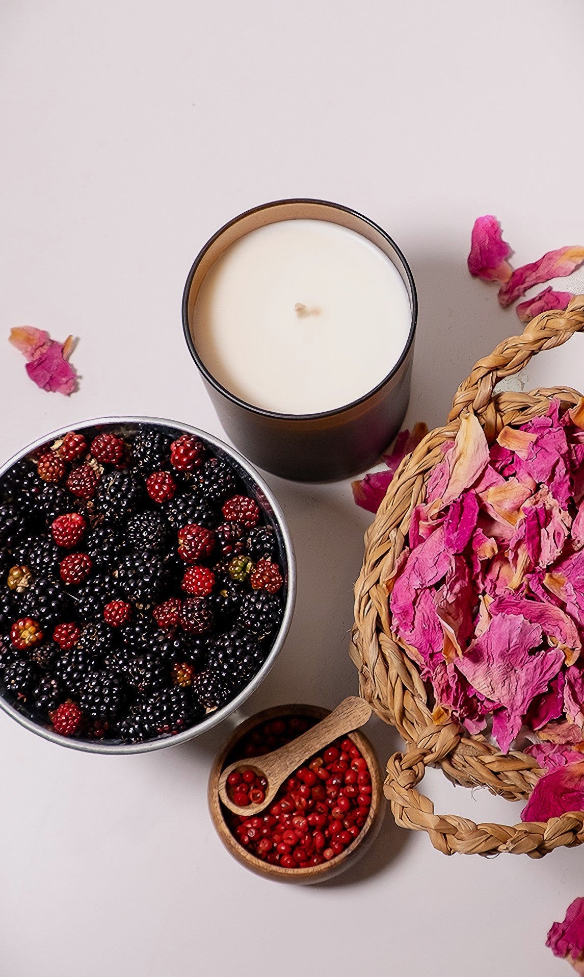 Candle with a bowl of berries, a basket of dried flowers, and a small bowl of red berries on a light background.