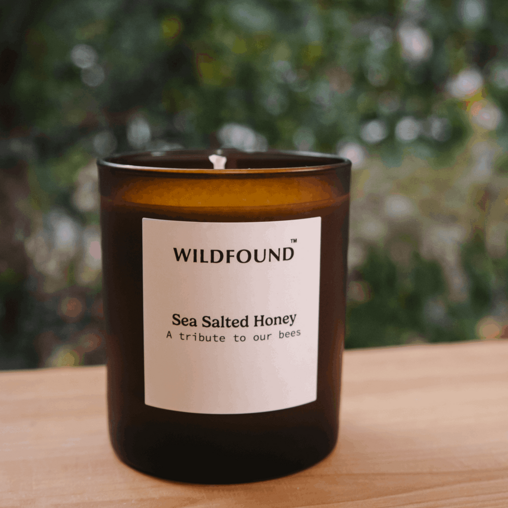 Candle with 'Wildfound' label on a wooden surface with blurred greenery in the background